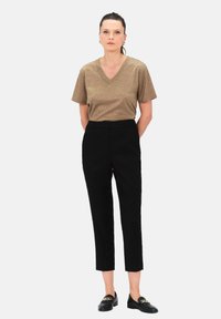 Miedziana bluzka z dekoltem w serek i krótkim rękawem, zestawiona z czarnymi spodniami o wysokim stanie i ściągaczami oraz czarnymi loafersami z akcentem w formie łańcucha.