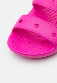 Růžové gumové skluzavkové sandály se dvěma širokými pásky s kulatými výřezy, texturovanou stélkou a hladkou podrážkou.