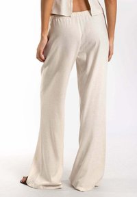 Pantalones de pierna ancha en beige, confeccionados en tejido ligero. Cuentan con una cinturilla elástica y una textura suave con un ligero brillo.