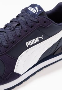 Baskets bleu marine avec une bande blanche sur le côté, une languette rembourrée et un tissu texturé. Logo Puma en blanc et lacets assortis.