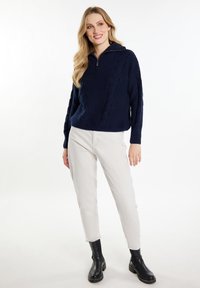Pulover negru cu împletitură în formă de cablu, cu guler rigat, asortat cu pantaloni de culoare deschisă și cizme negre până la gleznă. Design texturat și casual.