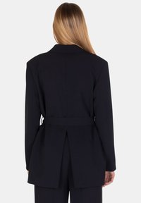 Blazer nero con una vestibilità sartoriale, dotato di uno spacco sul retro, una cintura e un colletto classico a rever. Texture liscia e design strutturato.