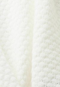 Tissu en tricot blanc texturé avec un motif en relief, offrant une apparence douce et duveteuse, tissé serré pour la chaleur et le confort.