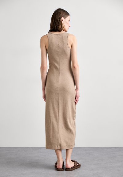 Abito midi beige aderente, con scollatura a barchetta, texture a coste e dettagli senza cuciture nella parte posteriore. Indossato con sandali intrecciati marroni.