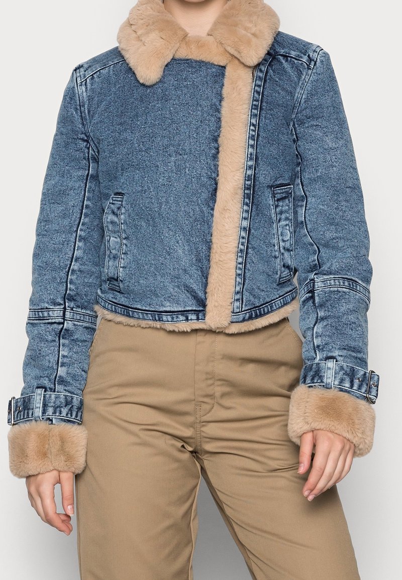 Chaqueta de mezclilla recortada con cuello y puños de piel sintética, con un lavado en azul claro, dos bolsillos laterales y botones decorativos en las mangas.