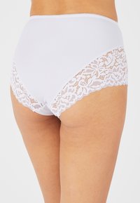 Hoge taille witte slipjes van zachte stof met doorschijnende witte kanten accents aan de zijkanten en gegolfde randen.