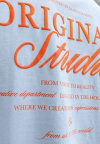 Λευκό ύφασμα με μεγάλο πορτοκαλί κείμενο «ORIGINAL Studio» και μικρότερες πορτοκαλί φράσεις για τη δημιουργικότητα και την τοποθεσία στην Κοπεγχάγη, Ολλανδία.