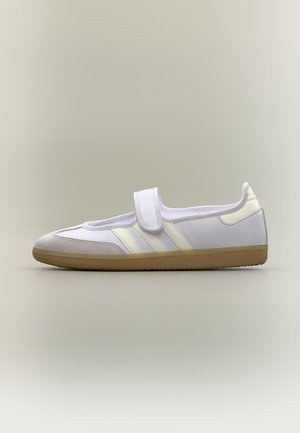 Baskets basses blanches et crème avec une seule bride Velcro et une semelle en caoutchouc marron clair, vues de côté sur un fond neutre.