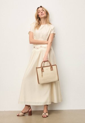 Lysebeige maxikjole med korte ærmer og blonder ved taljen, kombineret med en tan vævet håndtaske og brune hæle-sandaler.