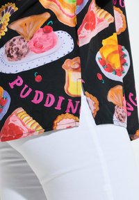 Tissu noir avec des illustrations colorées de desserts, dont glace, tarte, pudding et cerises sur un pantalon blanc.