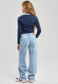 Jeans in denim azzurro chiaro con una vestibilità relax, dotati di un'etichetta in pelle sul retro, tasche laterali e pantaloni con risvolti, abbinati a una maglietta a maniche lunghe blu navy.
