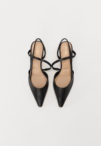 Talons aiguilles en cuir noir avec un design à dos nu et des sangles croisées. Semelles intérieures beige visibles, arborant le logo de la marque en or. Texture lisse.