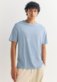Svijetloplava pamučna majica kratkih rukava s okruglim izrezom, glatke teksture i opuštenog kroja.