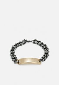 Pulseira de corrente com elos metálicos pretos e uma placa de latão dourada. Apresenta uma textura suave e bordas arredondadas na placa.