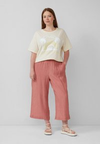Crème oversized T-shirt met een grafische print; koraalkleurige wijde broek; witte sandaaltjes met bandjes. Zachte texturen en een relaxte pasvorm.