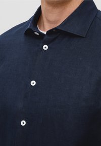 Camicia di lino blu navy con colletto a punta e dettaglio dei bottoni bianchi, caratterizzata da una superficie testurizzata e una vestibilità morbida.