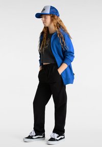 Blue zip-up hoodie, black cropped top, black jogger pants, and black sneakers. Hat is blue and white with a mesh back.