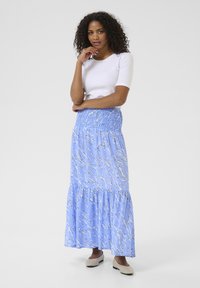 Jupe maxi bleu clair avec un motif abstrait blanc, dotée d'une taille froncée et d'un design à volants. Associée à un haut blanc à manches courtes.