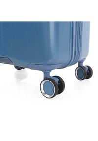 Maleta de viaje rígida azul con una superficie texturizada, que cuenta con cuatro ruedas negras con detalles en plata para facilitar la movilidad.