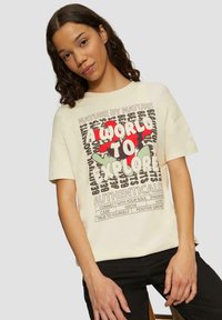 Crème t-shirt met een grafisch ontwerp met de tekst "EEN WERELD OM TE ONDERZOEKEN", omringd door bloemmotieven en motiverende zinnen, met korte mouwen.