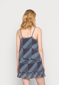 Marinblå mönstrad klänning med geometriska former i vitt och vinrött, med tunna spaghetti-remmar och en volangnederkant. Lättviktigt tyg.