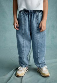 Ljust blå denim byxor i baggy-modell med elastisk midja, sidofickor och kontrasterande sömmar, kombinerat med flerfärgade sneakers.