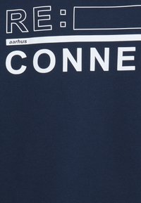 T-shirt en coton bleu marine avec texte en lettres blanches en bloc : "RE : CONNE" et "aarhus" avec un contour rectangulaire au-dessus du texte. Texture lisse.