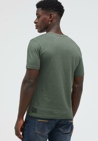 Green, short-sleeve T-shirt with a crew neck, made of lightweight fabric. Features a small black logo on the lower right side.
