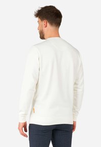 Vit sweatshirt med ribbade ärmslut och nederkant, slät textur, accentuerad av en liten orange etikett på sidan, visad bakifrån.