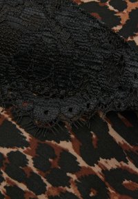 Czarny koronkowy wykończenie nakłada się na tkaninę w leopardzi wzór w odcieniach brązu i beżu. Koronka ma falbaniasty brzeg z wyciętymi detalami.