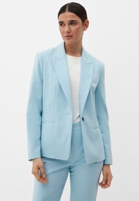 Blazer azzurro chiaro su misura con revers a regina, chiusura a un bottone e due tasche frontali, abbinato a una t-shirt bianca e pantaloni coordinati.
