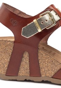 Bruine leren wedge sandaal met een kurken zool, voorzien van een metallic gouden gesp en een uitgesneden ontwerp op de bovenste band.
