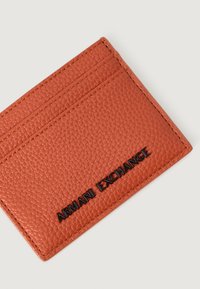 Tarjetero de cuero texturizado en color óxido con dos ranuras para tarjetas y el logo en negro "ARMANI EXCHANGE" en la parte frontal.