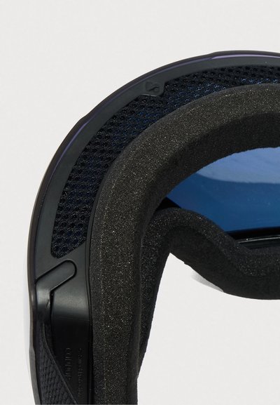 Posnetek v bližini črnega okvirja z penasto oblogo in modro obarvanim steklom zaščitnih športnih očal na belem ozadju.