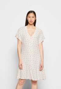 Vestido bege claro com decote em V, mangas curtas e bolinhas pretas. Apresenta um fechamento com botão e um design de saia rodada.