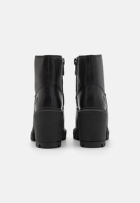 Botas de cuero negro hasta el tobillo con un tacón bloque alto, que cuentan con un cierre lateral y detalles texturizados en la parte posterior y los lados.
