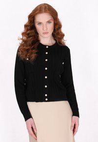 Cardigan nero a coste con scollatura rotonda, caratterizzato da grandi bottoni perla bianchi lungo la parte frontale e due tasche anteriori.