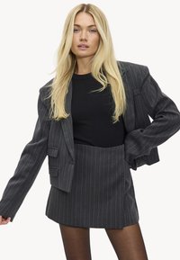 Blazer gris con rayas finas y corte holgado, combinado con una camiseta negra acanalada y una falda a juego. Textura suave y diseño entallado.