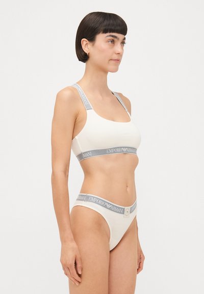 Light beige bra and panty set with gray elastic bands. The bra features wide straps, while the panties have a low-rise cut and logo detailing.