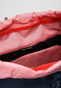 Wnętrze morskiej torby ma czerwono-białą paskowaną podszewkę, czarną kieszeń oraz metkę z napisem "Witamy w Herschel". Miękki materiał, ściągacz.