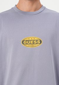 Grå bomull t-skjorte med en rund gul og grønn "GUESS ORIGINALS" logo på brystet, med design for klassisk rund hals.