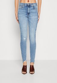 Jeans skinny de tiro alto en azul claro con detalles de rasgadura en las rodillas y dobladillo deshilachado. Combinados con sandalias de tacón burdeos, de punta abierta y con un acabado brillante.