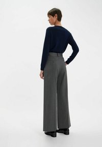 Haut à manches longues bleu marine avec un col rond, associé à un pantalon grise à rayures verticales, à taille haute et à jambes larges, avec un détail de poche arrière.
