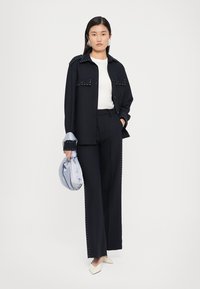 Navy button-up shirt with studded details, white t-shirt, tailored dark pants, cream pointed shoes, and light blue bag, set against a white background.