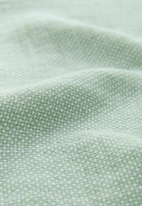Tejido texturizado de color verde claro con un patrón tejido, que presenta pequeños cuadrados y un acabado suave y liso. Ideal para tapicería o prendas de vestir.