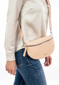 Persikofärgad lädercrossbody-väska med rundad form, silverfärgad dragkedja och justerbar rem. Texturerad yta med minimalistisk design.