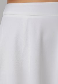 Jupe blanche avec un tissu lisse et texturé, présentant un design légèrement drapé et une large ceinture, offrant une silhouette fluide.