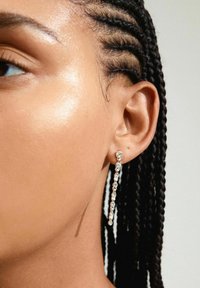 Silberohrringe mit einem linearen Design, die mehrere klare Kristalle aufweisen, die in einer zarten Kette herabfallen. Glatte Textur, minimalistischer Stil.