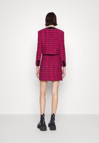 Rosa tweedjacka och mini-klänning, med långa ärmar och svarta detaljer. Texturerad tyg med en strukturerad silhuett. Svarta stövlar synliga.