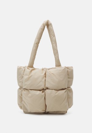 Bolso tote beige acolchado con dos asas acolchadas, que presenta una superficie suave y texturizada y una forma cuadrada con cuadros cosidos visibles.